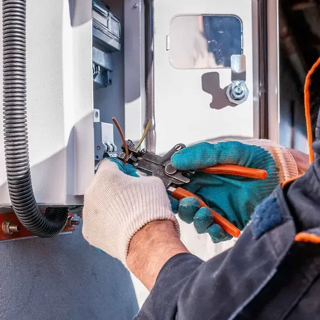 Un hombre está trabajando en una caja eléctrica con alicates.