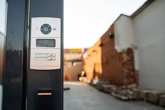 Un primer plano de un timbre en una valla con un edificio de ladrillos al fondo.