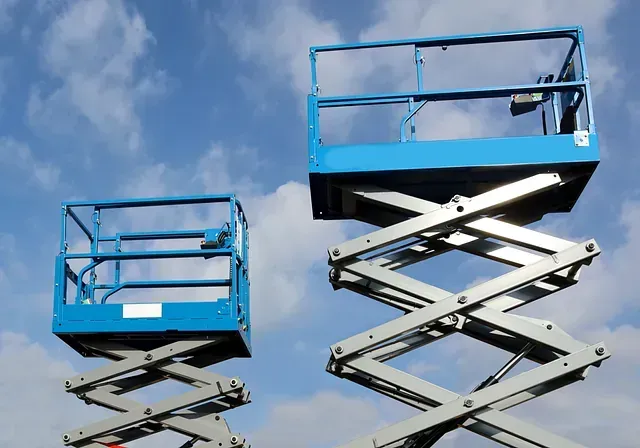 Dos elevadores de tijera contra un cielo azul con nubes