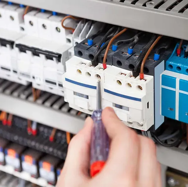 Una persona está trabajando en un panel eléctrico con un destornillador.
