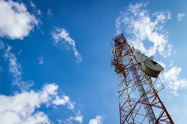 Una torre telefónica con una antena parabólica encima contra un cielo azul con nubes.