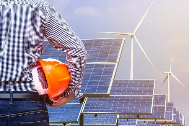 Un hombre sostiene un casco delante de una fila de paneles solares y turbinas eólicas.