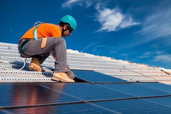 Un hombre está instalando paneles solares en el tejado de un edificio.