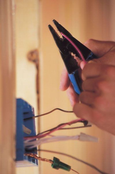 Una persona está trabajando en una toma de corriente eléctrica con unos alicates.