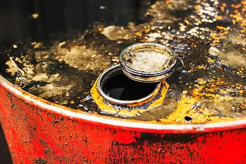 Un primer plano de un barril de petróleo oxidado con la tapa abierta.