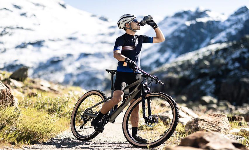 Eine Person trinkt Wasser, während sie mit dem Fahrrad auf einem Wanderweg unterwegs ist | PS Cycling AG