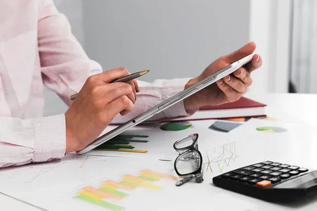 Una mujer está sentada en un escritorio usando una tableta y una calculadora.
