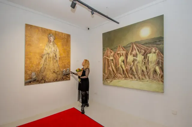 Una mujer está parada en una habitación con dos pinturas en la pared.