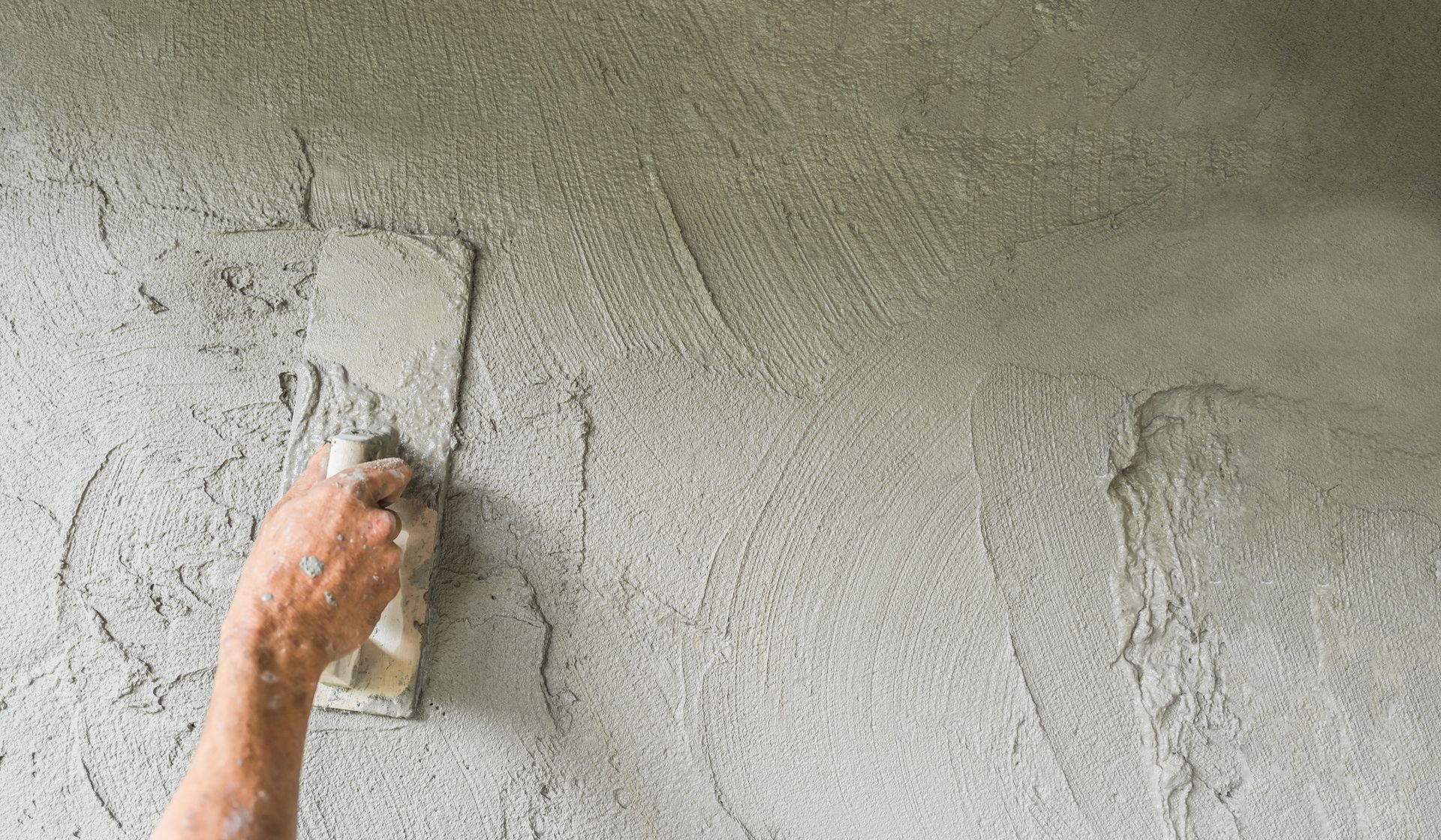 Lissage manuel d'un enduit gris humide sur un mur à l'aide d'une truelle.