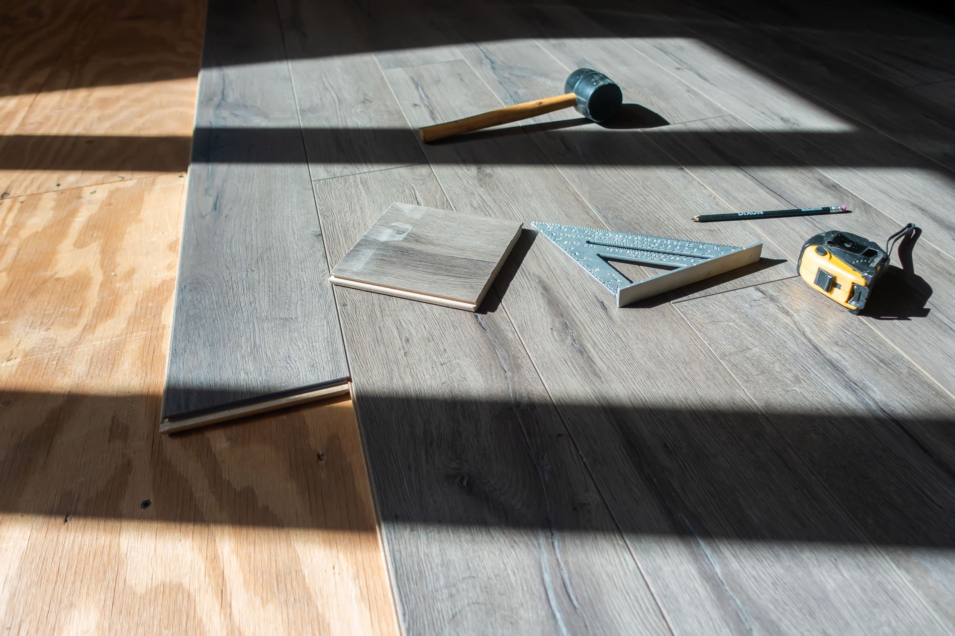 Outils de pose de moquette sur un sol gris en plein soleil, avec une genouillère bleue et un mètre ruban.