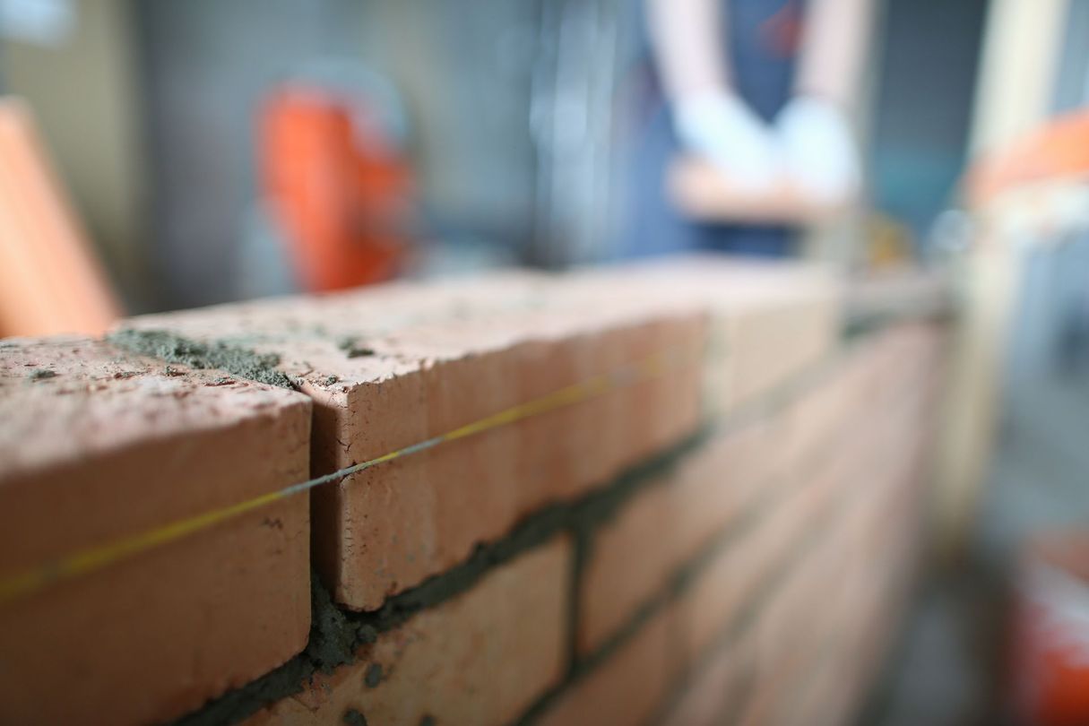 Gros plan sur un mur de briques en construction, avec des ouvriers et des outils flous en arrière-plan.