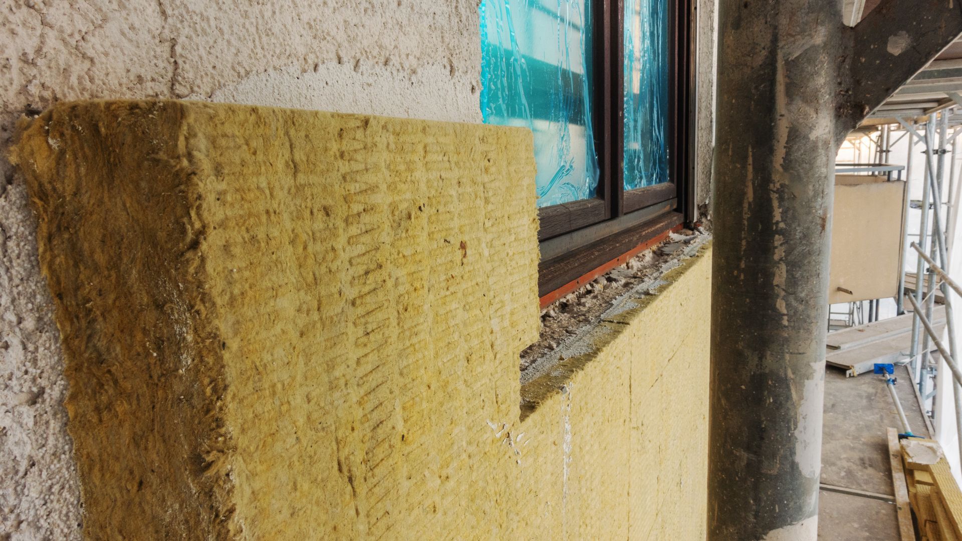 Gros plan sur l'extérieur d'un bâtiment avec un mur texturé jaune, une fenêtre et un échafaudage à côté.