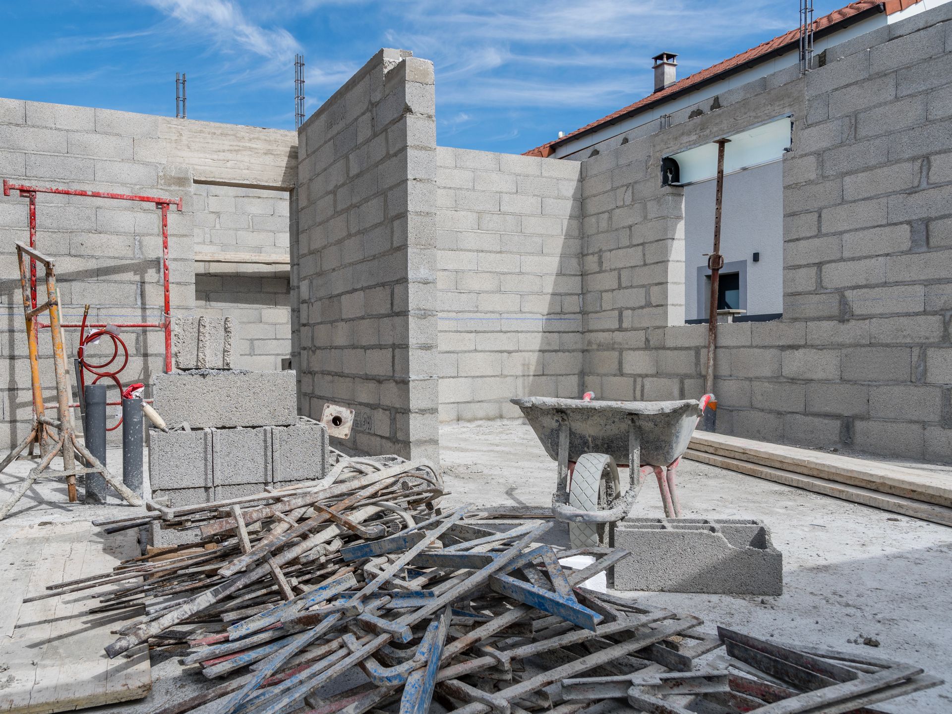 Maison en parpaings partiellement construite, avec échafaudages et débris de construction sous un ciel bleu.