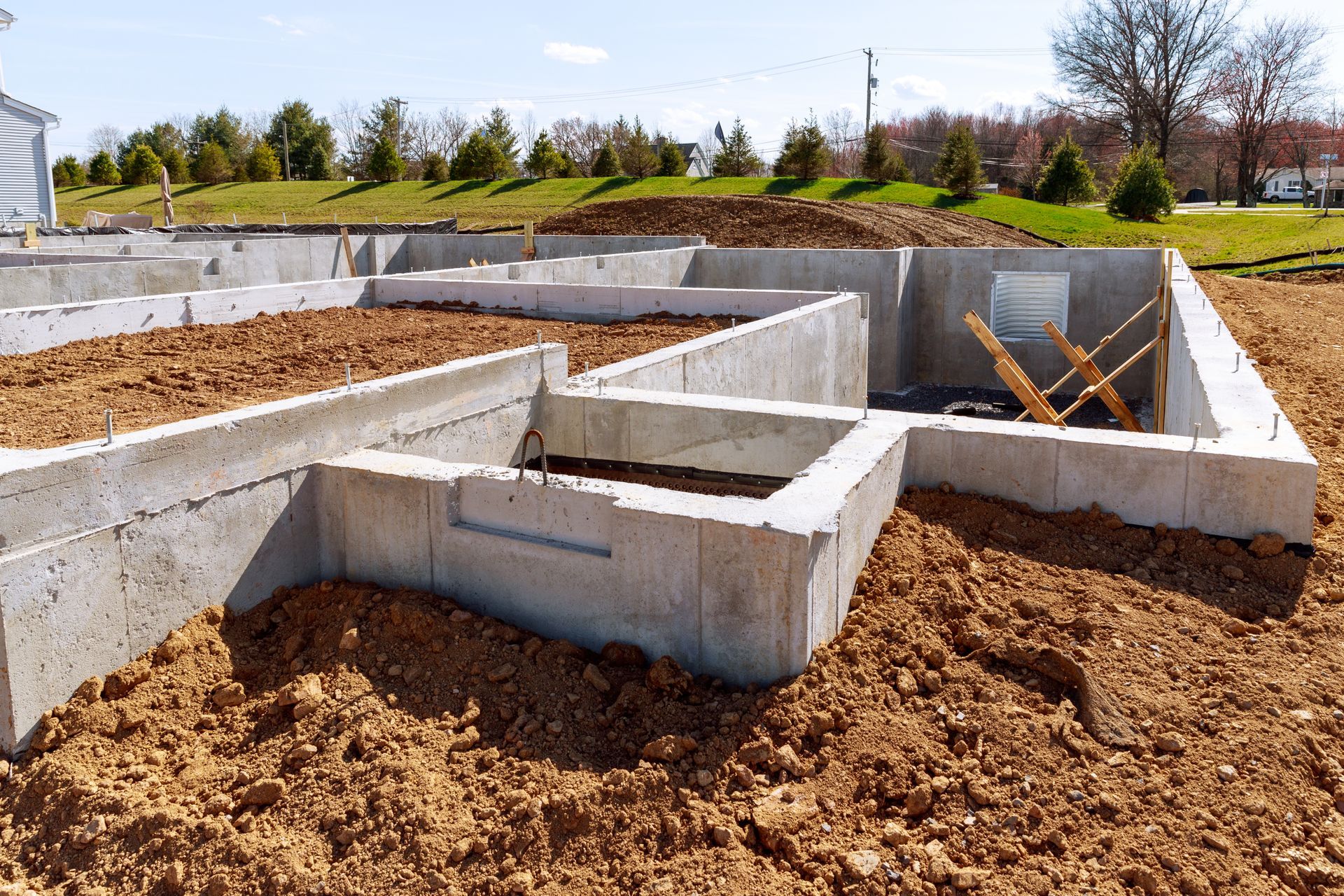 Murs de fondation et semelles en béton sur un chantier de construction, entourés de terre.