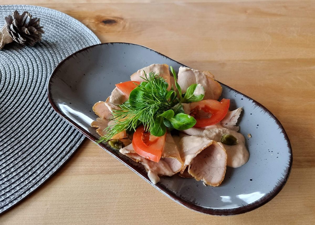 Aufgeschnittenes Fleisch mit Kirschtomaten und Petersilie auf einem schwarzen ovalen Teller auf einem Holztisch