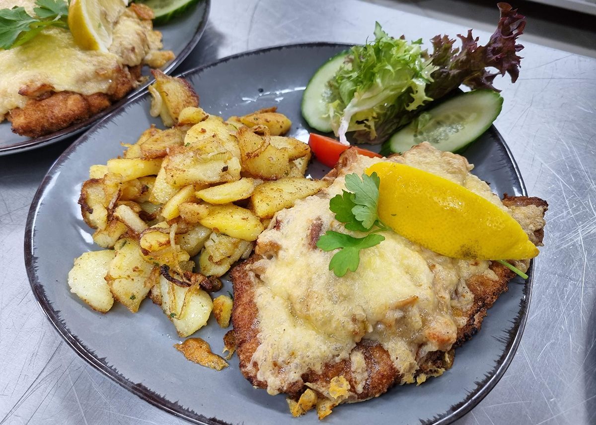 Zwei panierte Tellergerichte mit Pommes frites, Salat und Zitronenspalte auf einem Tisch.