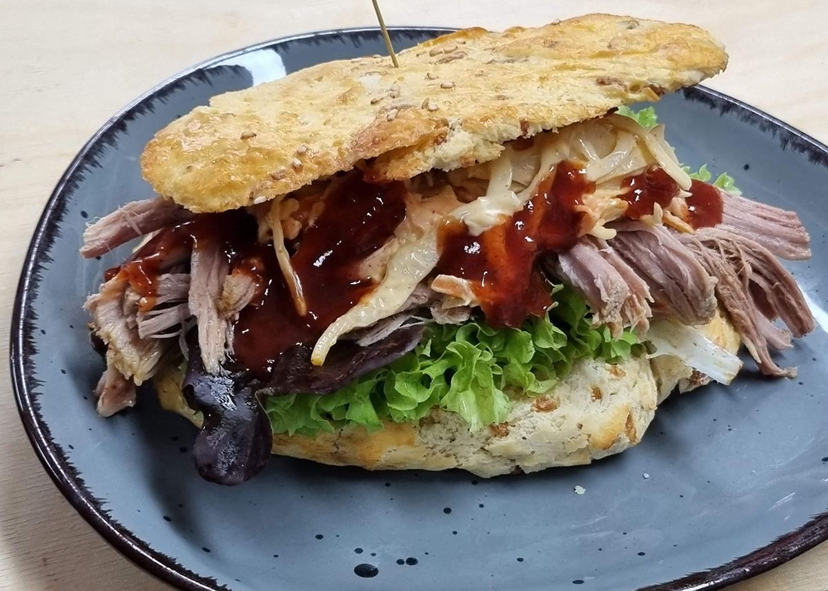 Großes Sandwich mit Salat, Fleisch und Soße auf einem grauen Teller