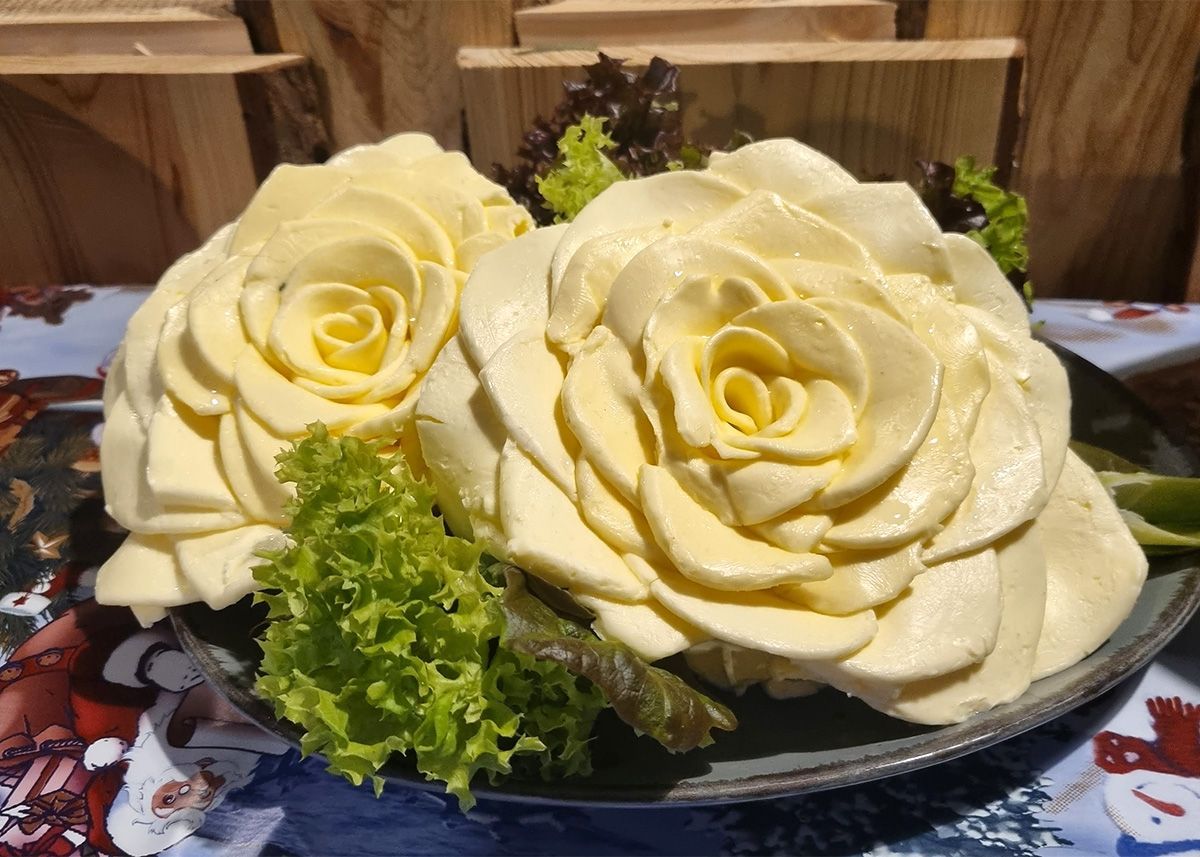 Zwei cremefarbene, rosenförmige Desserts mit grüner Garnierung auf einer Platte