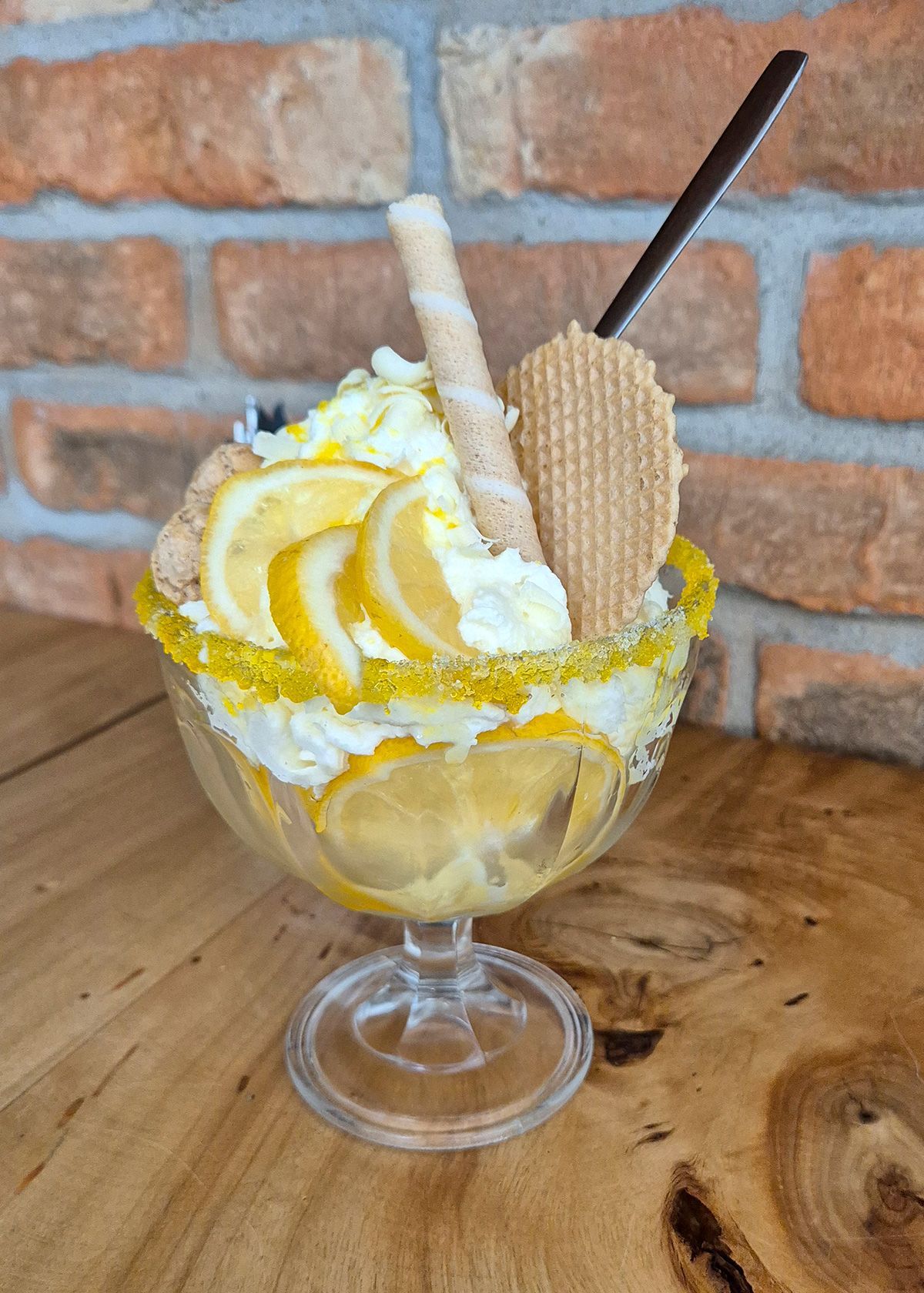 Eisbecher in einer Glasschale mit Waffelstäbchen und gelbem Sirup auf einem Holztisch