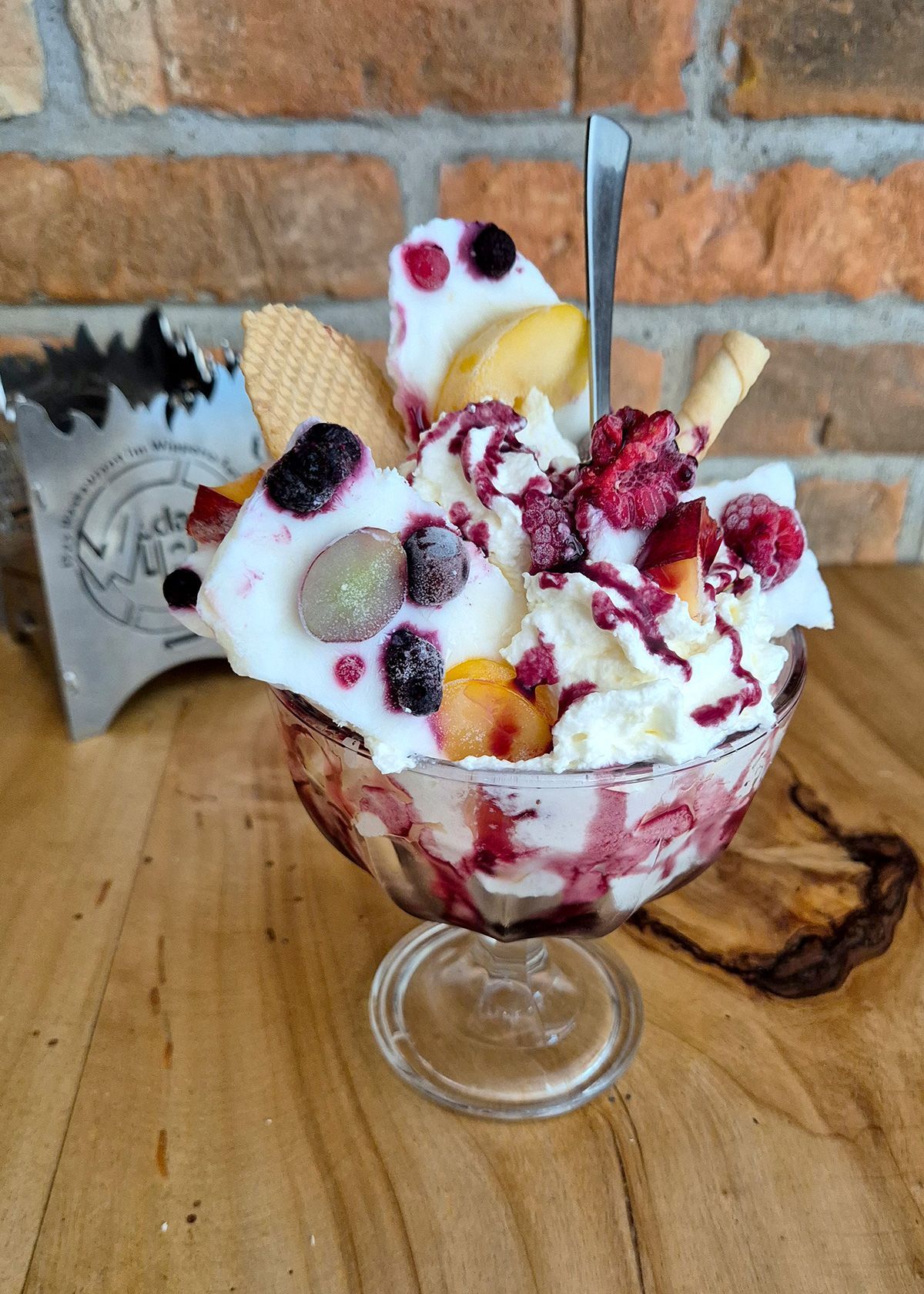 Eisbecher mit Beeren in einem Dessertglas auf einem Holztisch vor einer Backsteinmauer