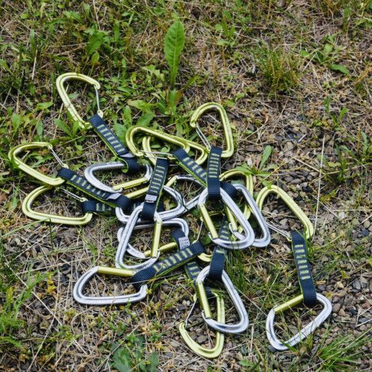 Eine Ansammlung grün-blauer Metallkarabiner, verstreut auf Gras und Erde.