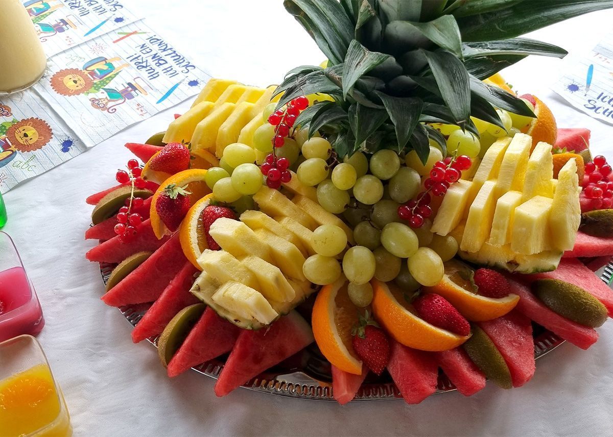 Obstplatte mit Ananas, Erdbeeren, Weintrauben, Kiwi und Orangenscheiben, arrangiert wie eine Ananaskrone.