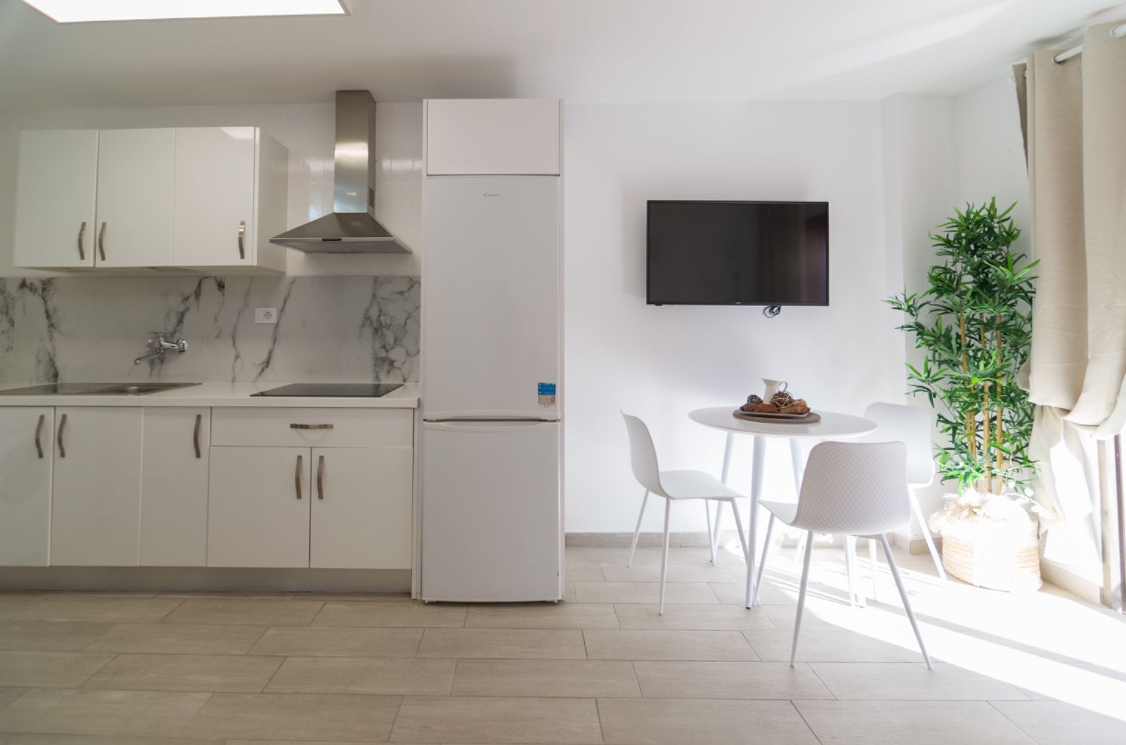 Una cocina con gabinetes blancos, un refrigerador, una mesa y sillas.