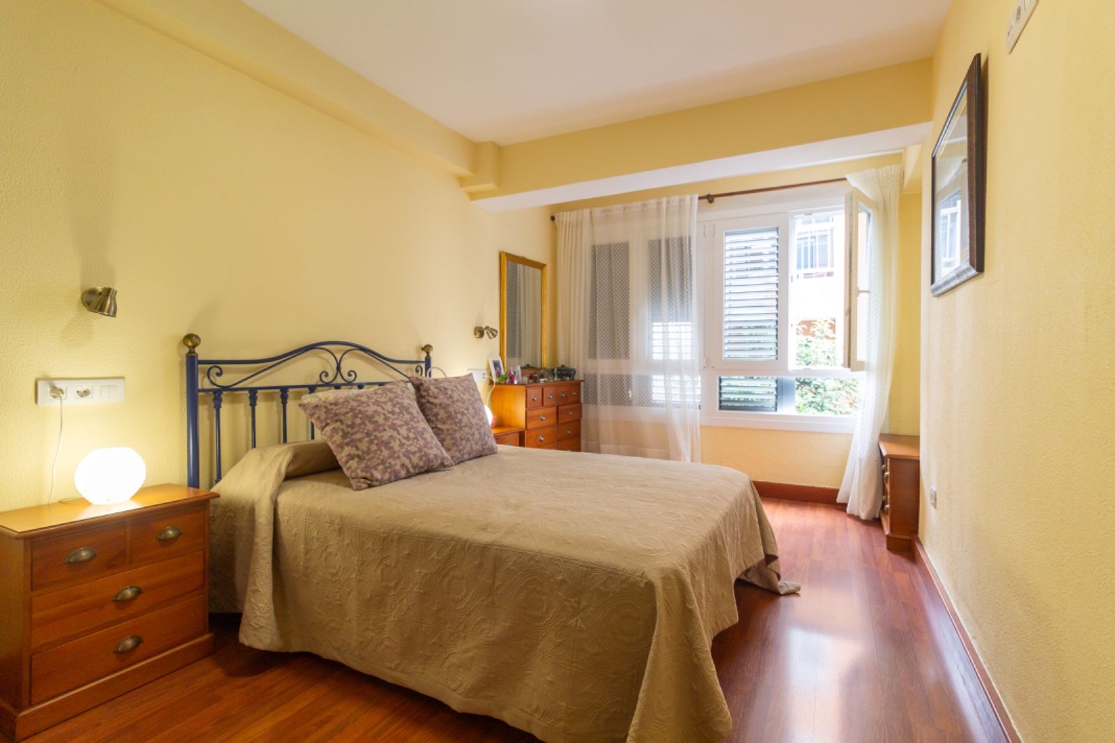 Un dormitorio con cama, mesita de noche, espejo y ventana.