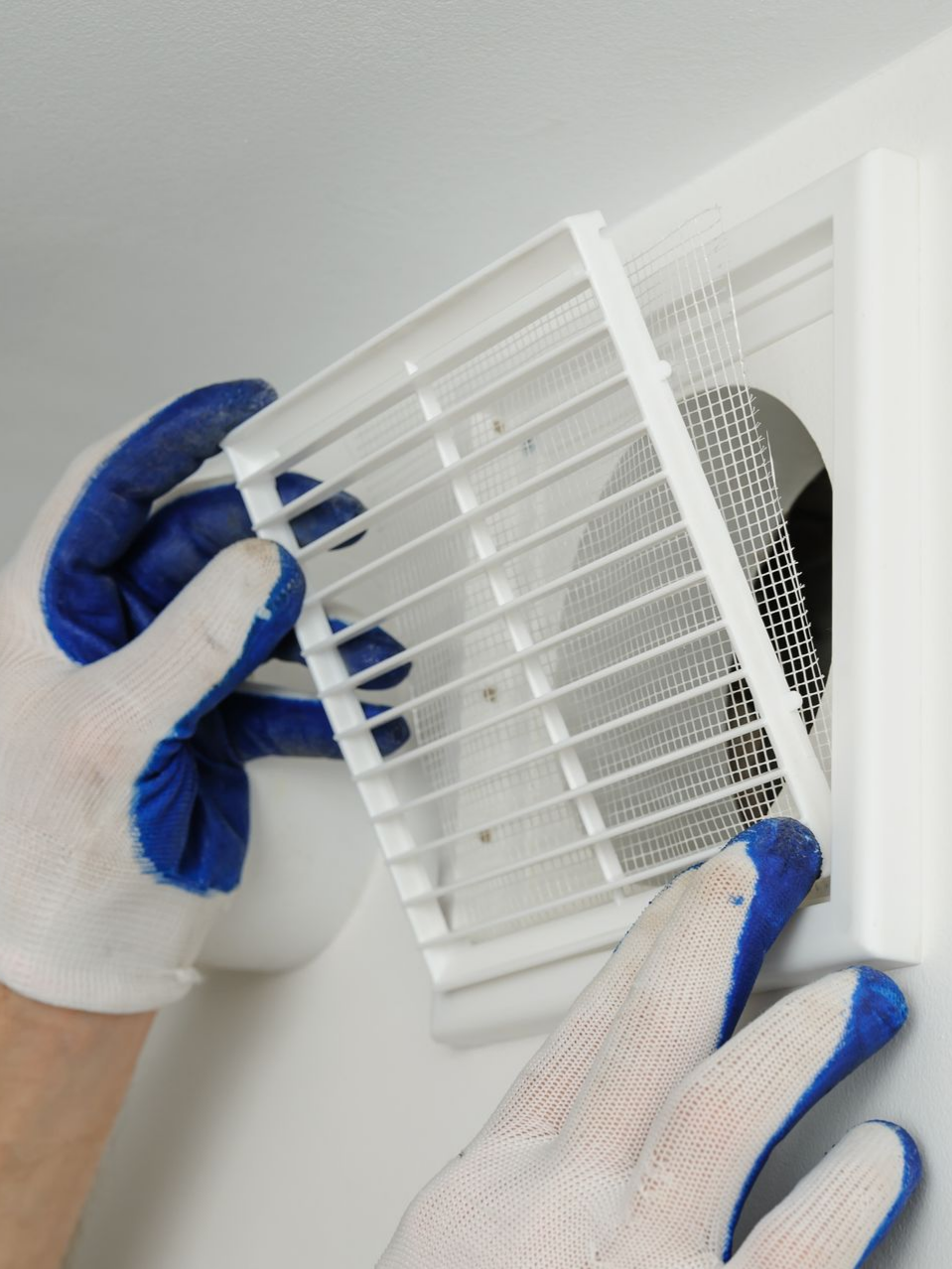 Des mains gantées installent une grille d'aération blanche sur un mur.