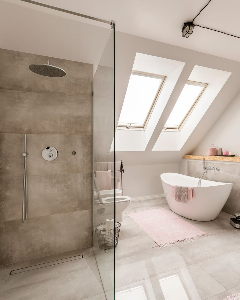 Salle de bains moderne avec douche et baignoire îlot. Carrelage gris, douche en verre, puits de lumière, tapis rose.
