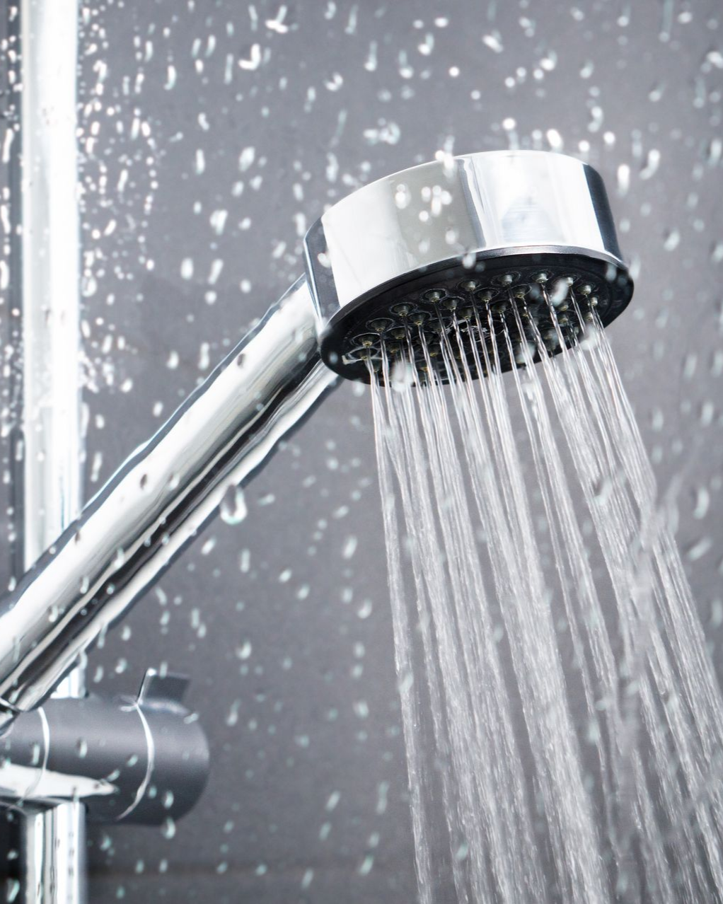 Pommeau de douche crachant de l'eau contre un mur carrelé foncé.