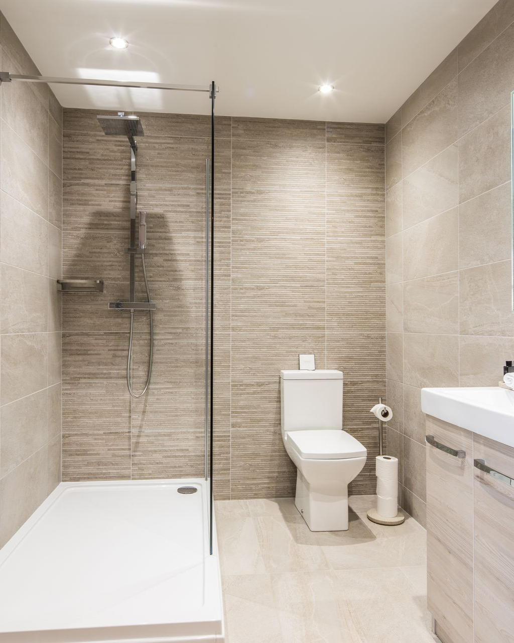 Salle de bains avec murs carrelés, cabine de douche, toilettes et meuble lavabo.