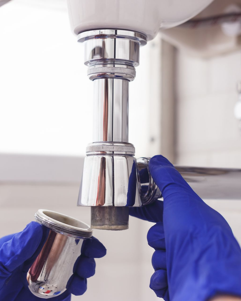 Des mains gantées de bleu, en train de démonter une bonde d'évier chromée.