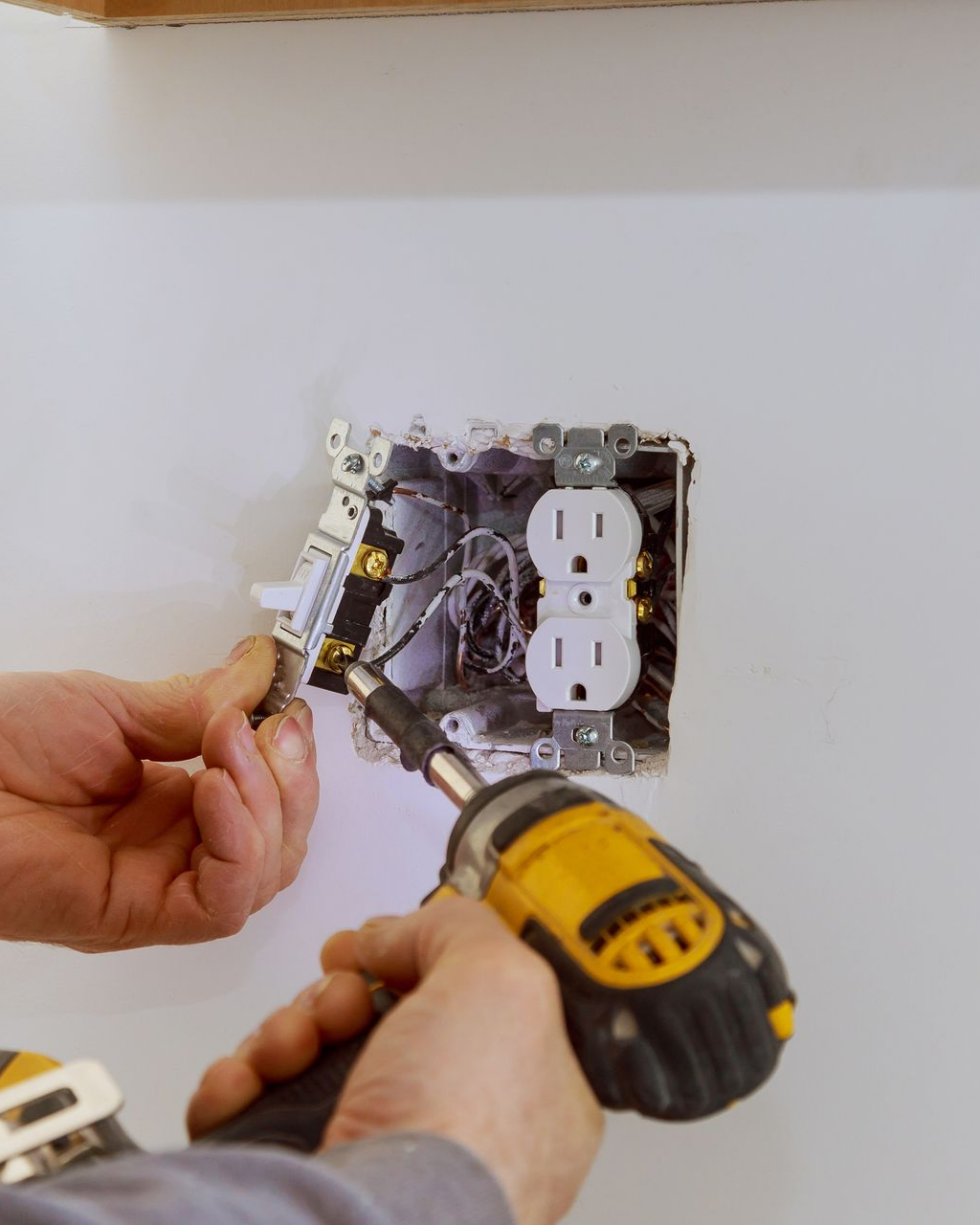 Une personne installe une prise électrique à l'aide d'une perceuse dans un mur blanc.