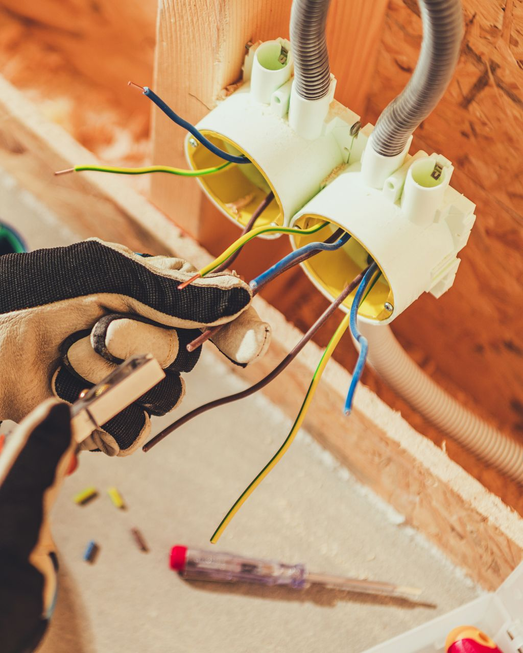 Un électricien portant des gants travaille sur des fils électriques dans un mur.
