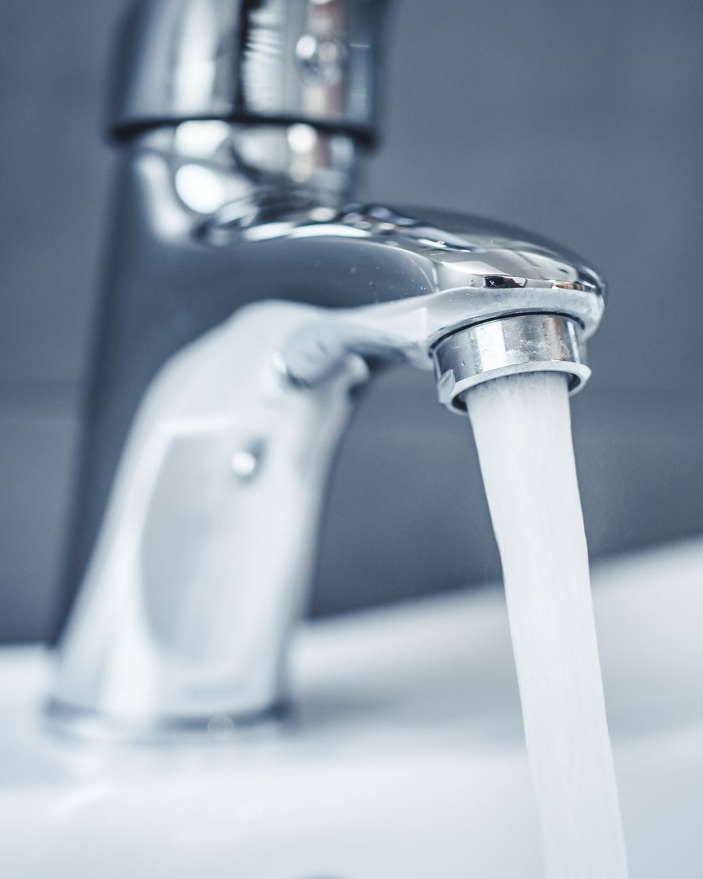 Robinet chromé d'où l'eau s'écoule dans un évier blanc.