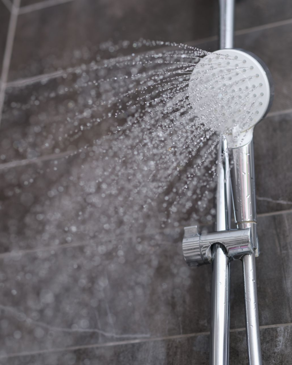 Pommeau de douche crachant de l'eau ; sur un fond de carrelage foncé.