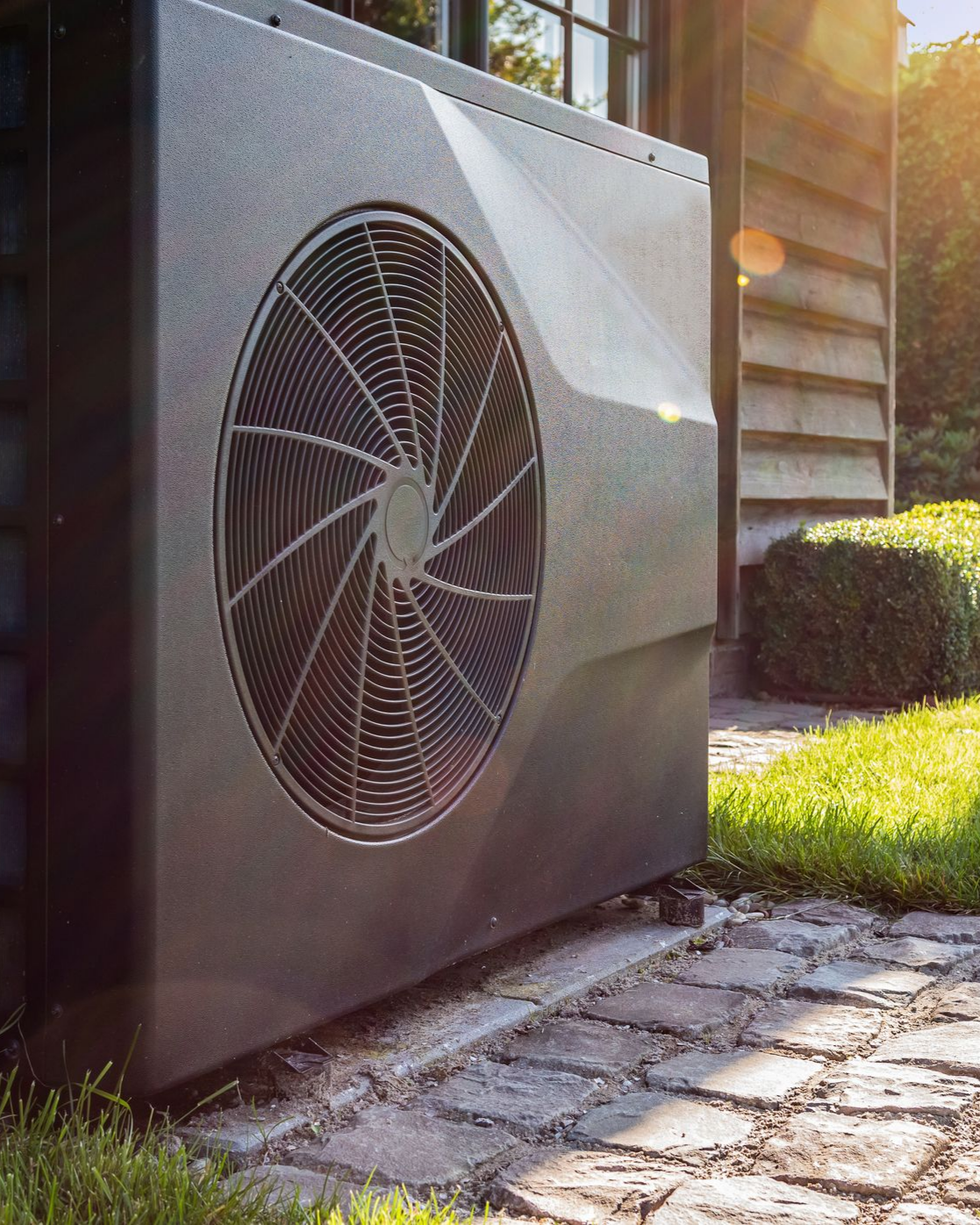 Unité de pompe à chaleur gris foncé à l'extérieur d'une maison, avec un ventilateur à l'avant.