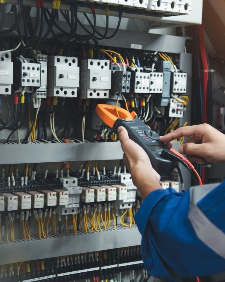Un électricien utilise un multimètre pour inspecter le câblage électrique d'un panneau de commande.