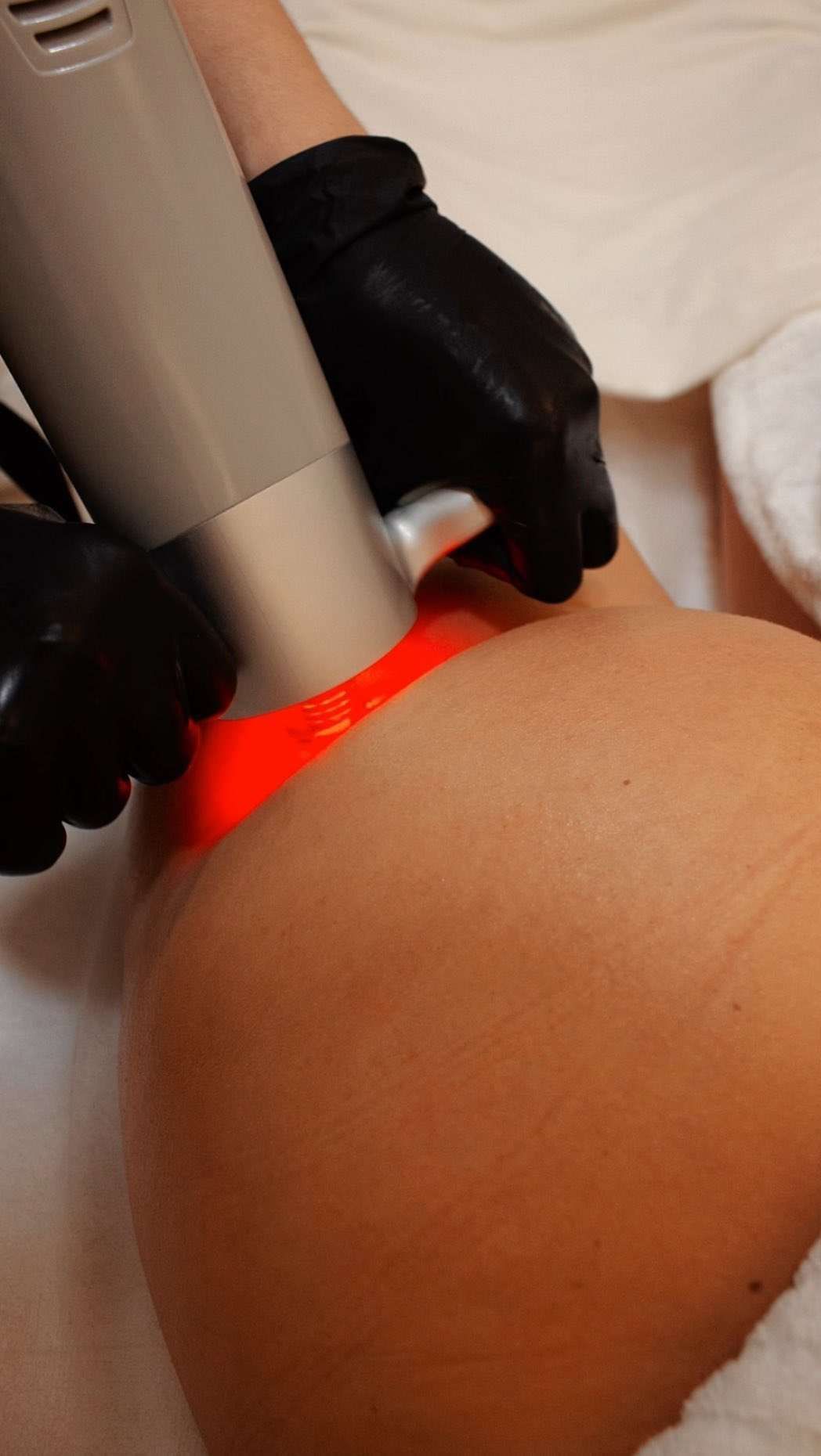 Una persona que lleva un guante negro aplica terapia de luz roja en un tratamiento corporal.