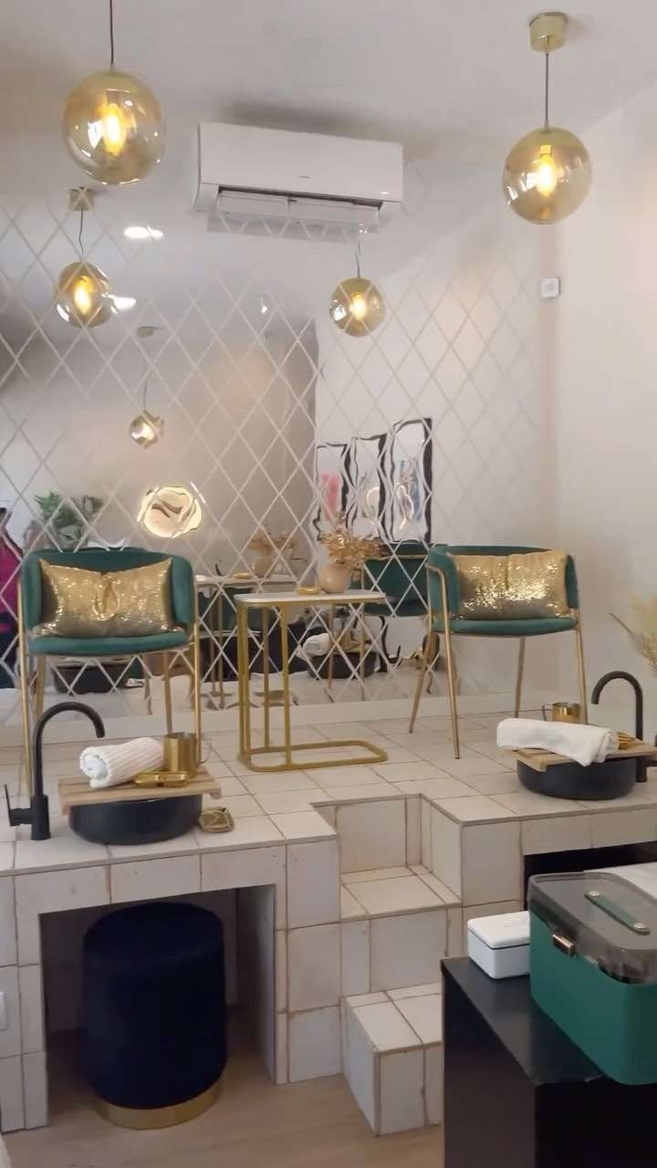 Interior de un salón de uñas con detalles dorados, sillas color verde azulado y spa para pies sobre plataformas blancas.