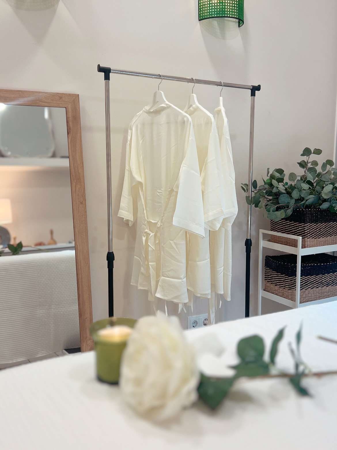 Un perchero con dos prendas color crema en un espacio bien iluminado. Al fondo se aprecia un espejo y elementos decorativos.