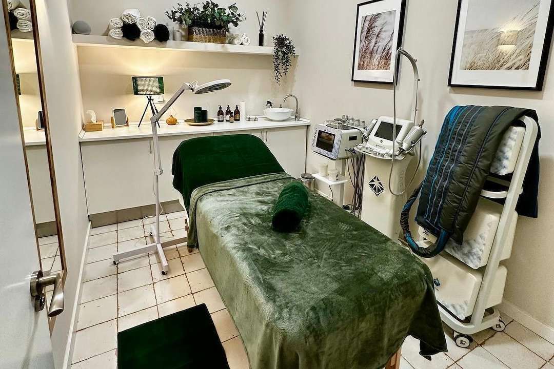 Sala de tratamientos de spa con cama verde, equipo médico y estantes decorativos.