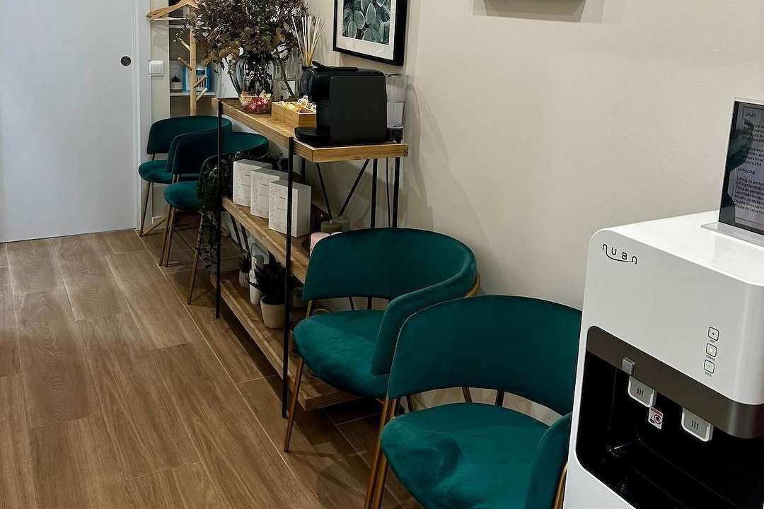 Zona de espera con sillas color verde azulado, estantes de madera y dispensador de agua.