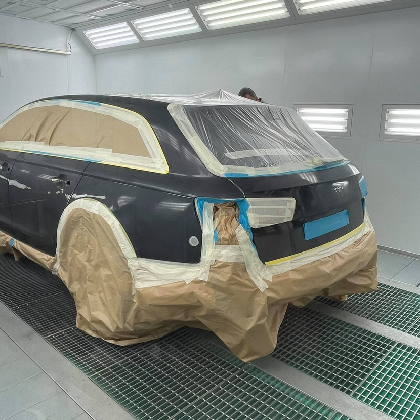 Voiture noire dans une cabine de peinture, masquée et préparée pour la peinture.