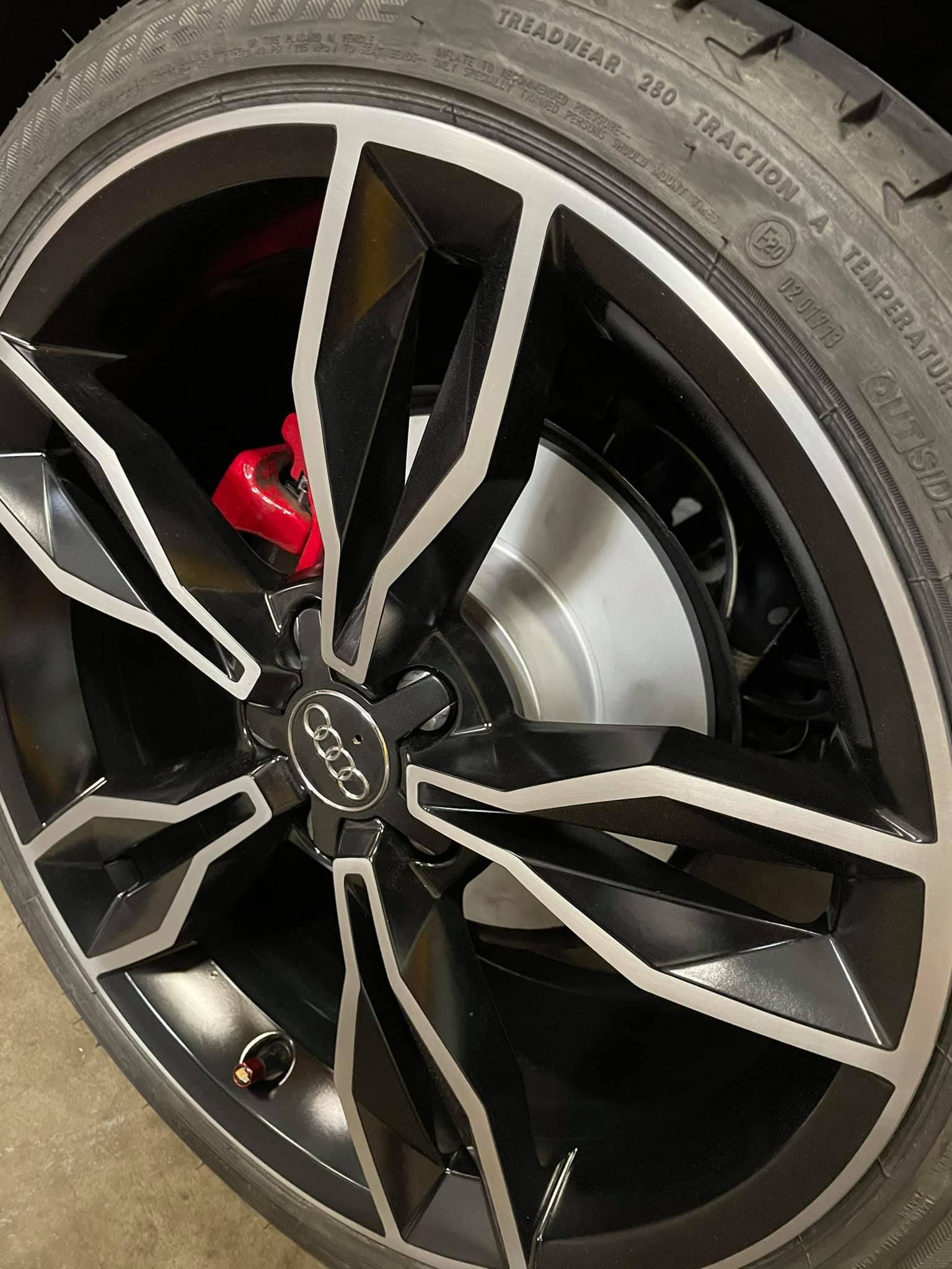 Gros plan d'une roue noire et argentée avec un étrier de frein rouge.