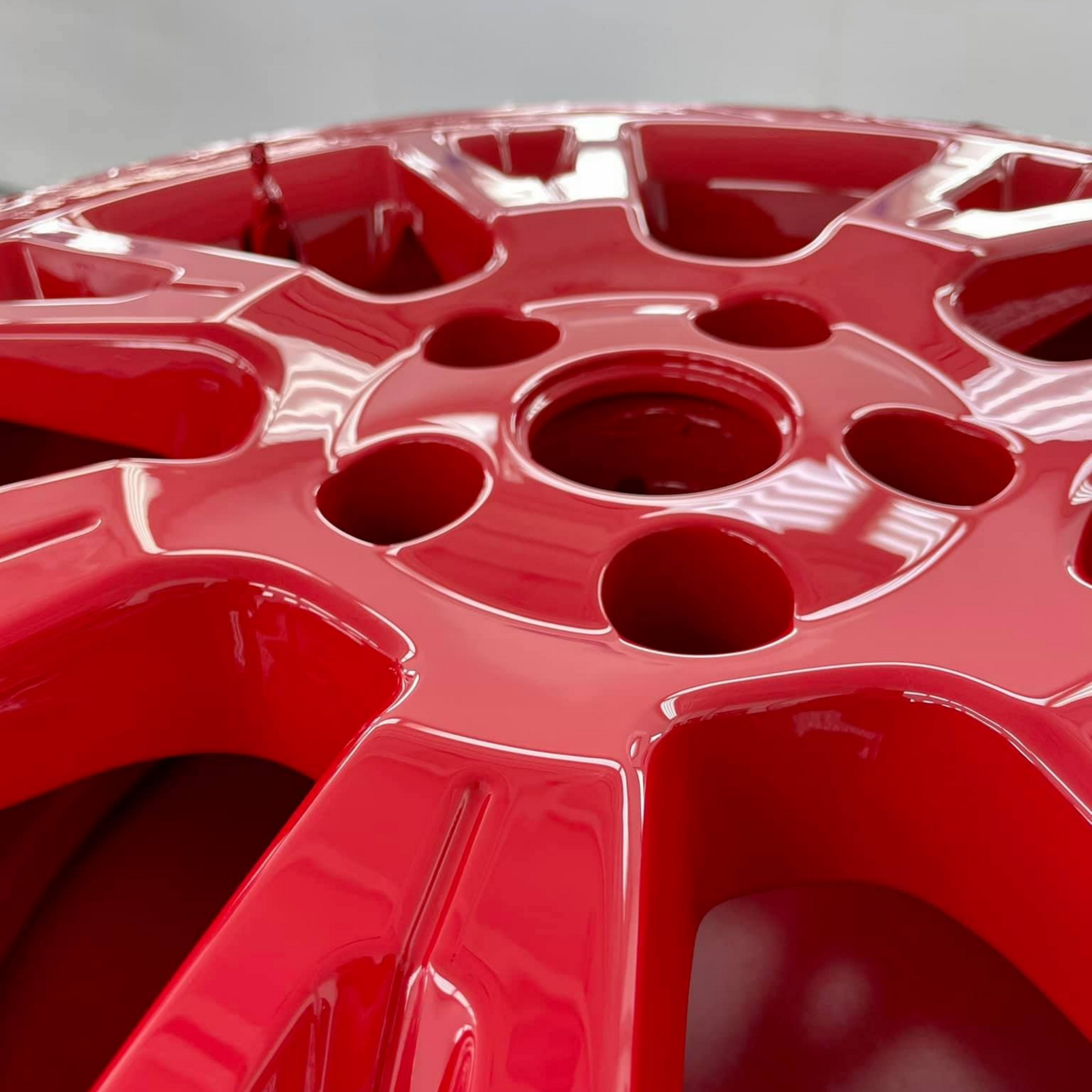 Gros plan d'une jante de voiture rouge brillante avec plusieurs ouvertures circulaires.