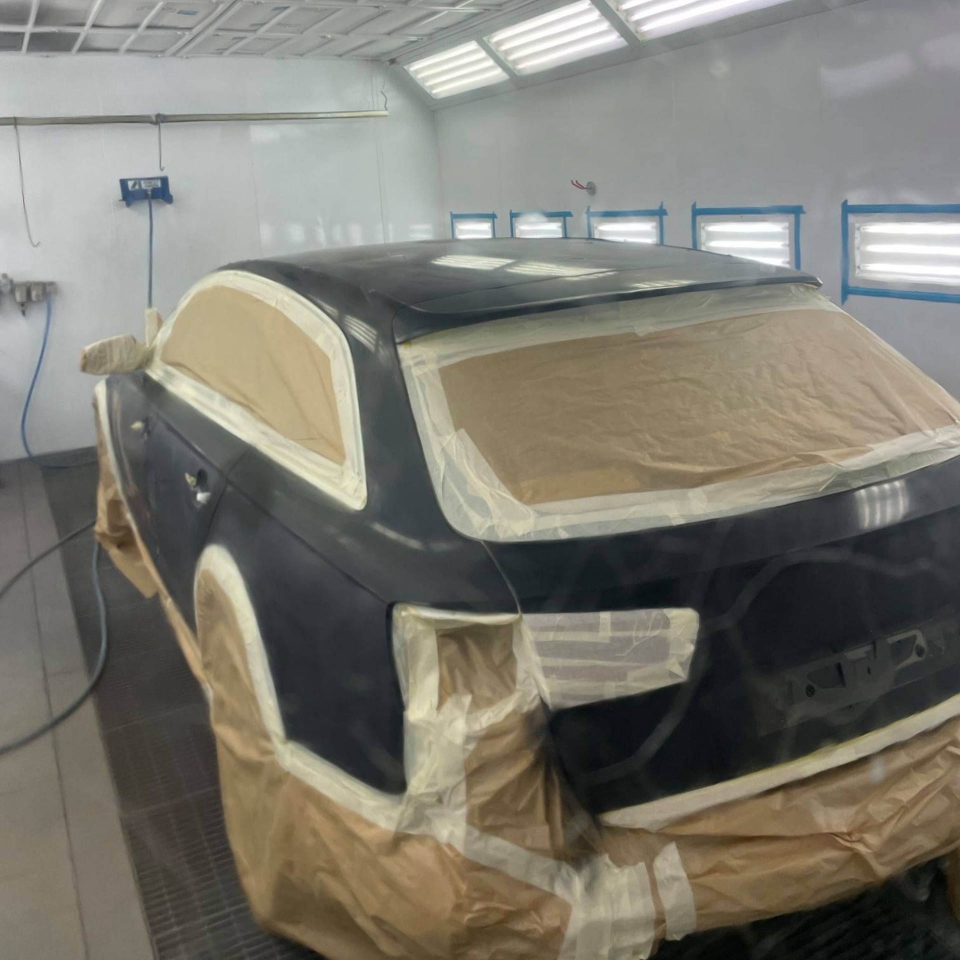 Voiture dans une cabine de peinture, masquée pour la peinture. Peinture bleu foncé, murs blancs, lumières vives.