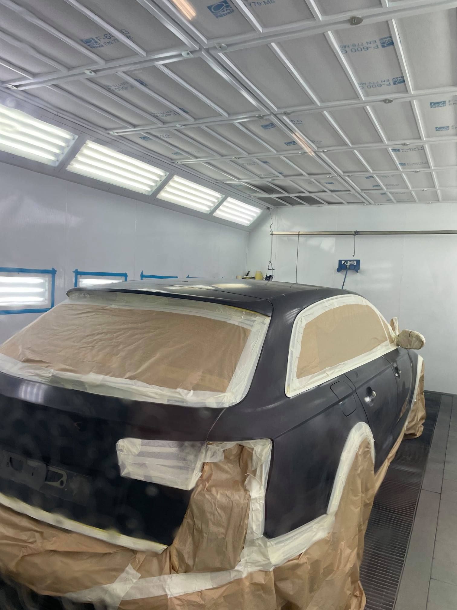 Voiture noire recouverte de ruban adhésif pour la peinture dans un atelier de carrosserie très éclairé.