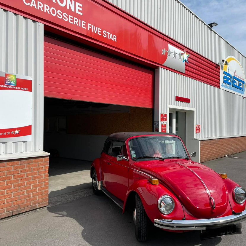 Voiture classique rouge garée devant un atelier de réparation automobile avec porte de garage rouge.